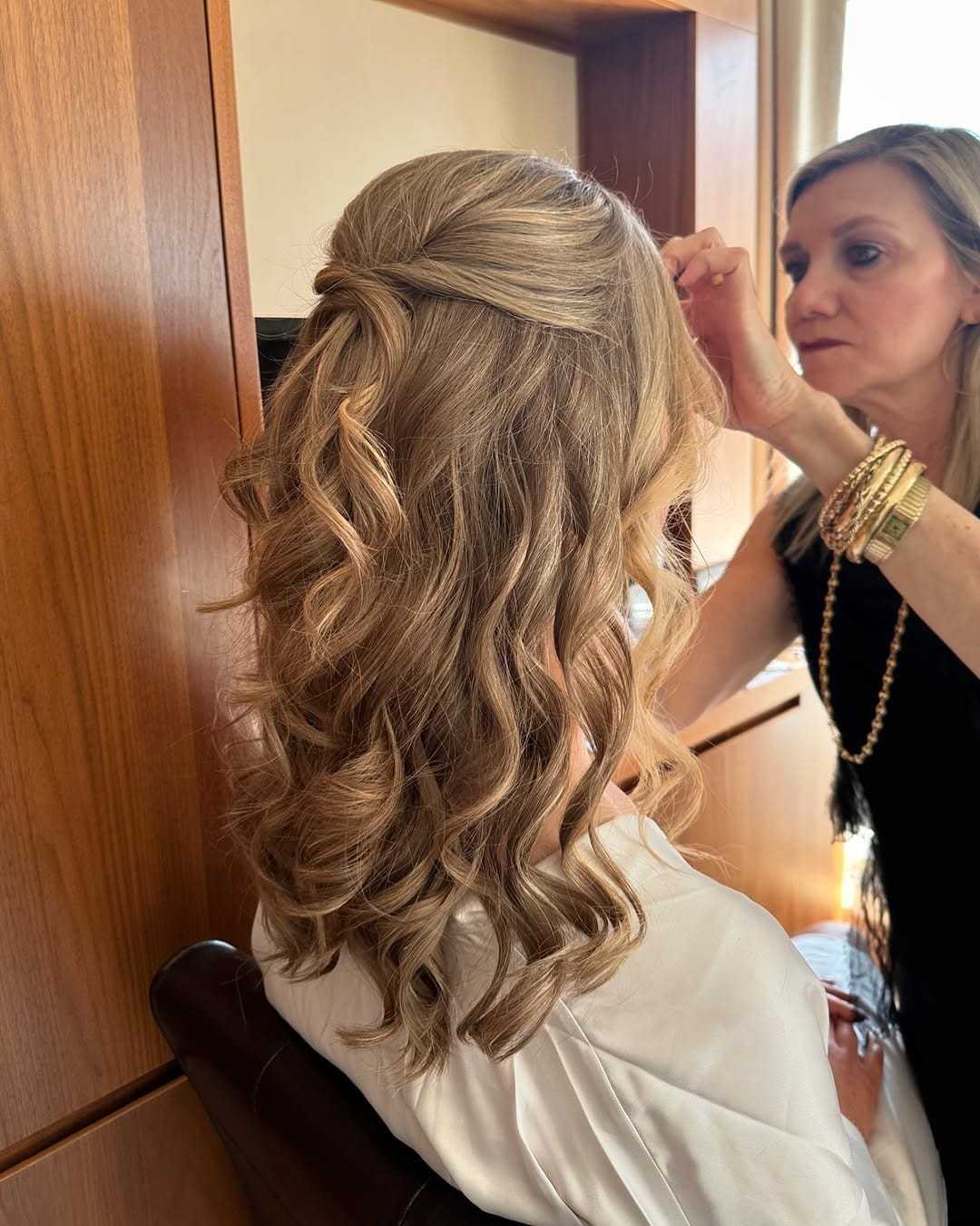 Person styling a woman's wavy blonde hair in a salon setting.