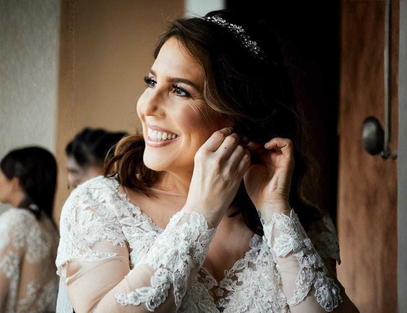 Bride smiling while adjusting earrings, wearing a lace wedding dress and tiara.