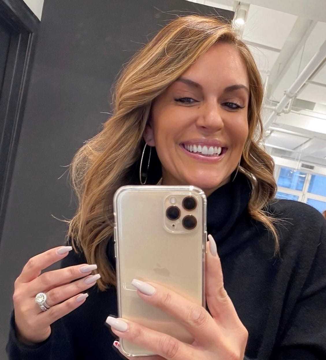 Woman taking a selfie with a smartphone, smiling in a well-lit room.