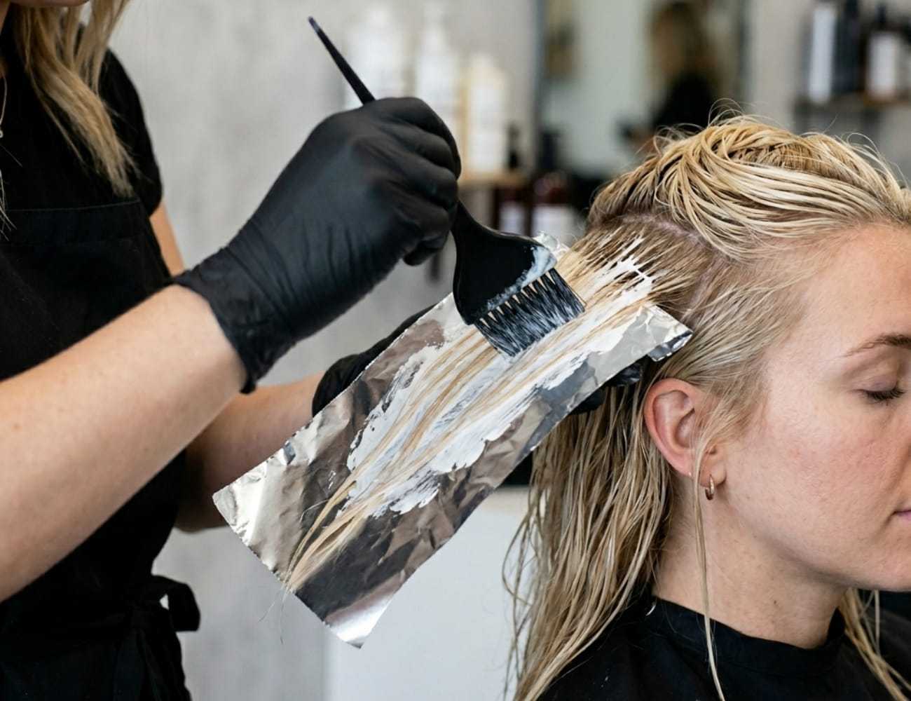 Hair stylist applying foil highlights to a client's wet hair in a salon setting.