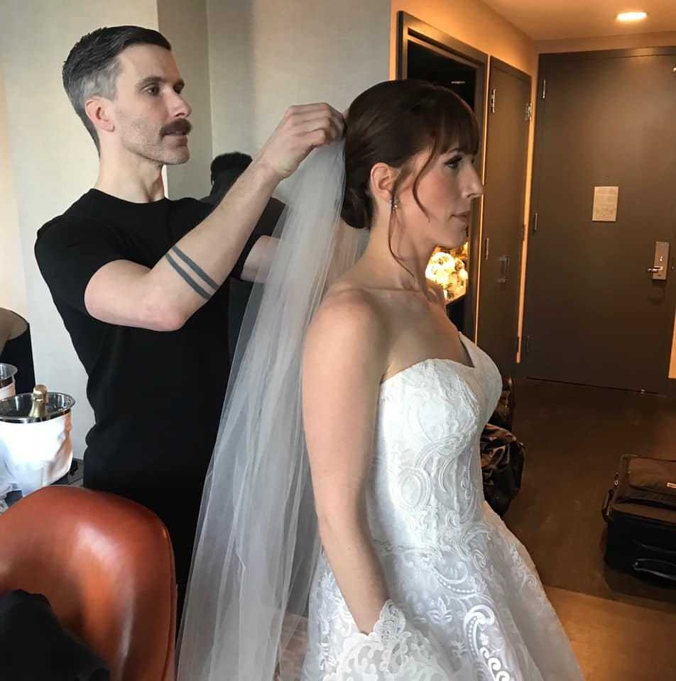 Bride getting ready as stylist adjusts her veil in a dressing room.