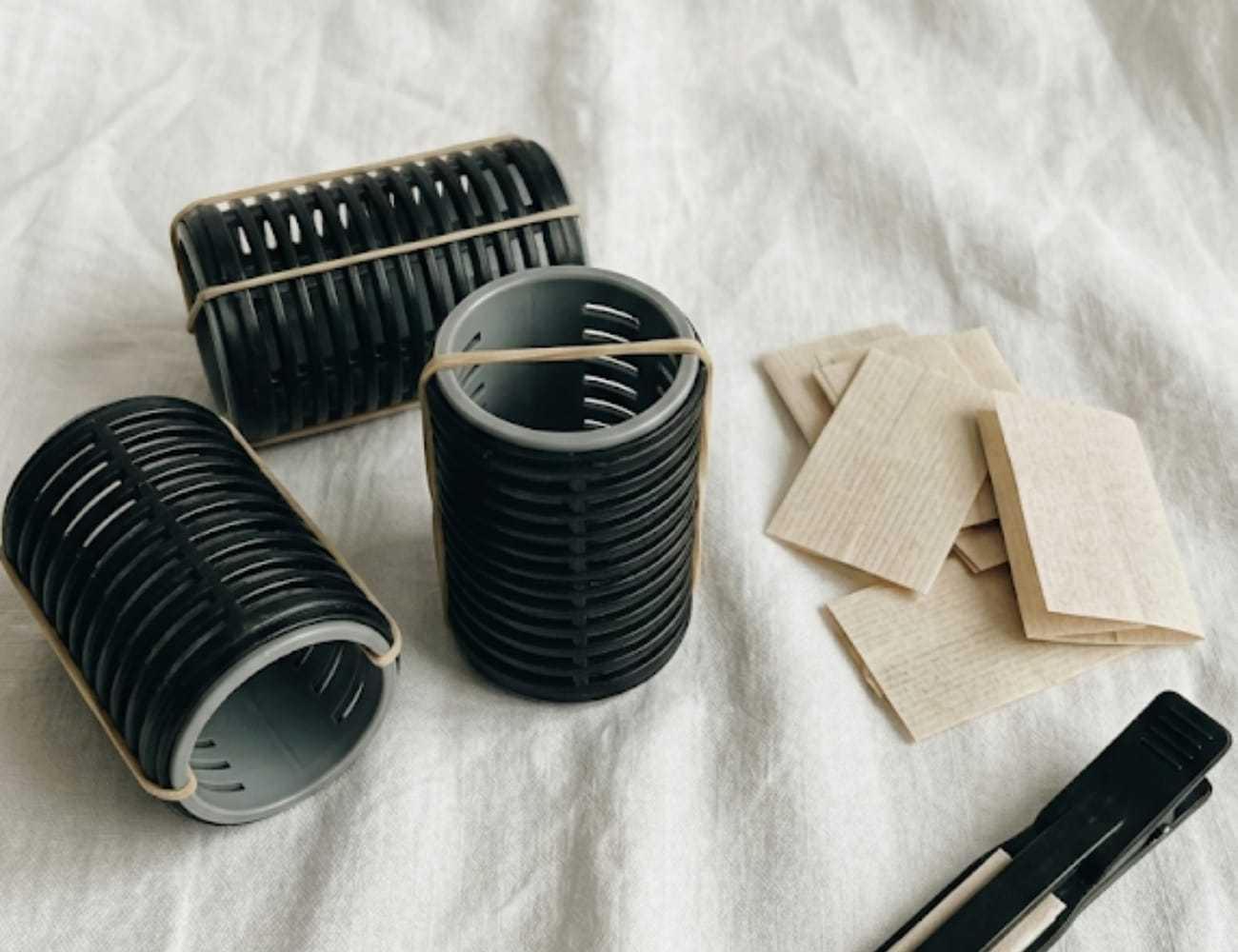 Heatless hair curlers, clips, and papers on a white fabric background.