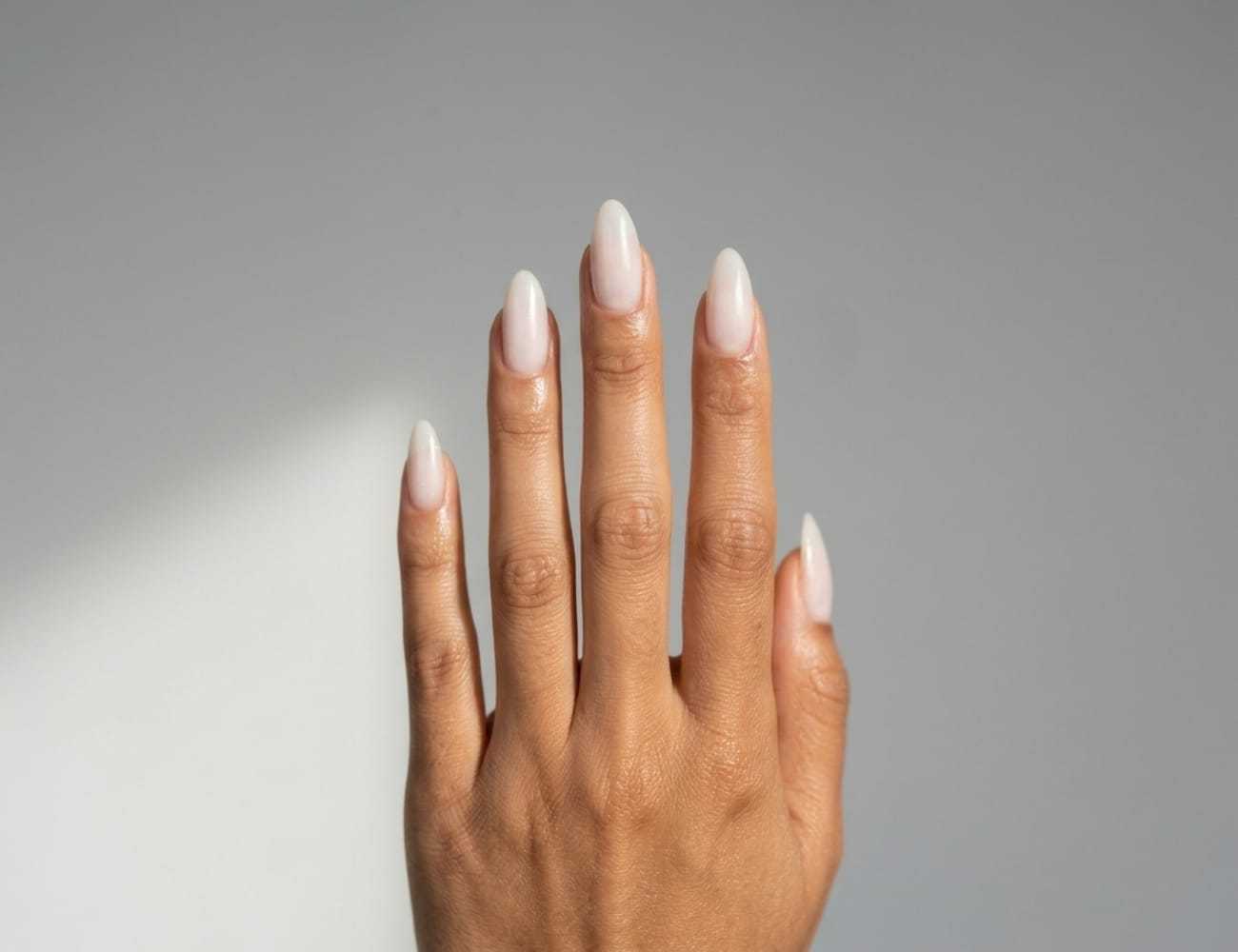 Manicured hand with long, almond-shaped nails against a light gray background.
